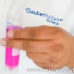 Persona con bata de laboratorio sosteniendo un tubo de ensayo con líquido rosa, fotografía corporativa para empresa química