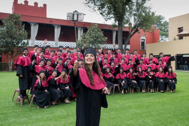 Generación de graduados con toga granate posando en el jardín del campus durante su sesión de fotos de graduación