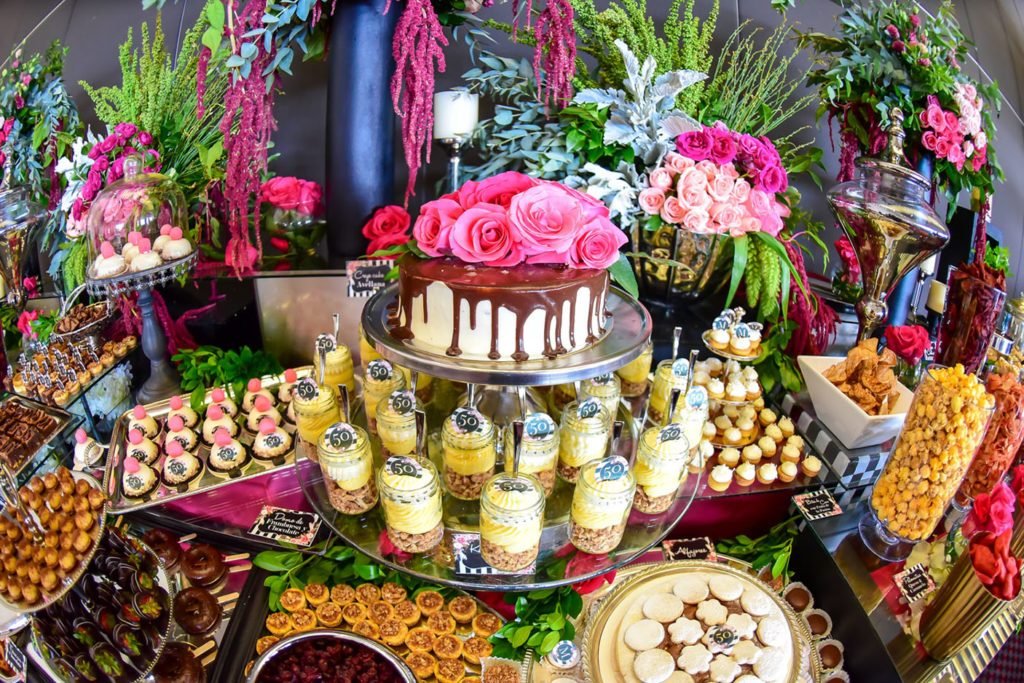 Mesa de postres de un evento con pastel de rosas, macarons y arreglos florales